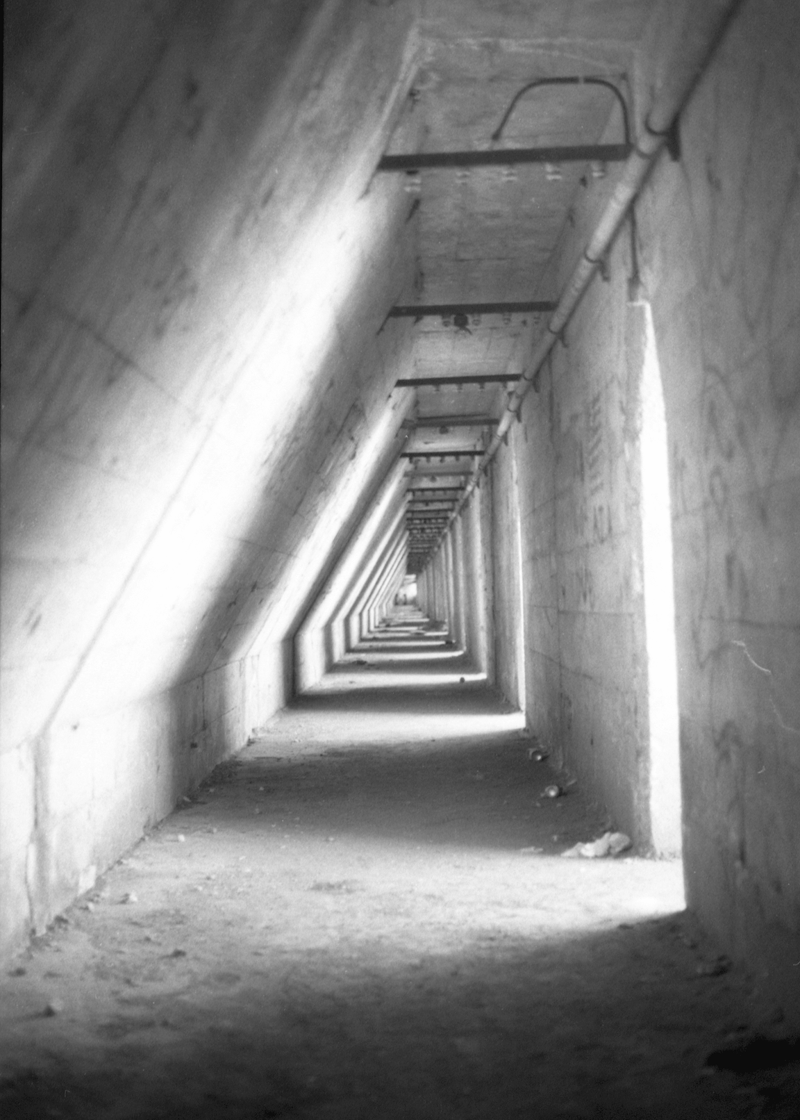 A black-and-white photo of a corridor, intermittently lit by sunlight beaming through open spaces.